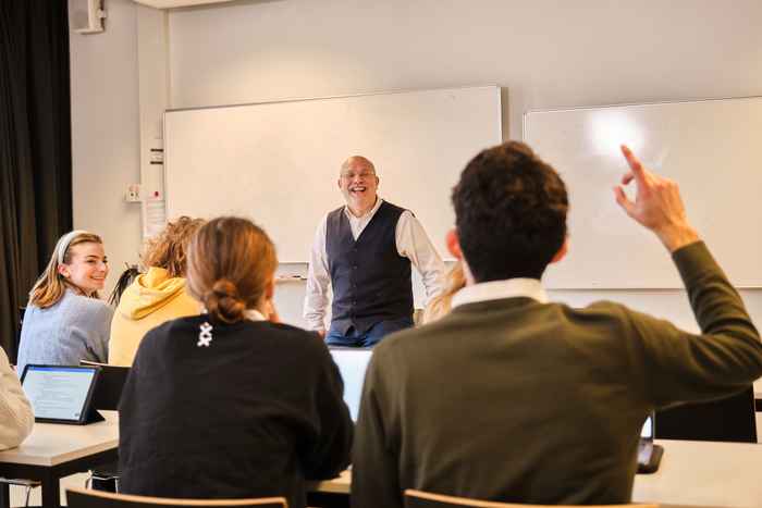 Student raising his hand with lecturer in front of the room